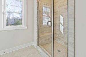 Bright bathroom featuring a glass-enclosed shower with tiled walls and floor, adjacent to a window with outside view.