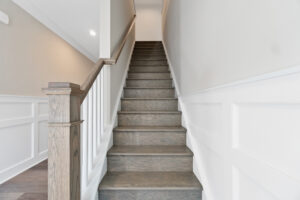 A wooden staircase with white paneling on the walls, leading upward in a well-lit interior space.