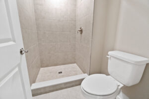 Bathroom with a tiled walk-in shower and a white toilet. Beige walls and a white door are visible.