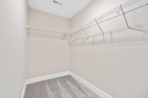Empty walk-in closet with beige walls, white trim, and wire shelving on two sides. The floor is gray and speckled.