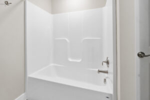 White, modern bathroom featuring a shower-tub combo with a silver faucet, white walls, and a silver towel bar on the left.