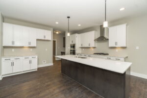 Modern kitchen with white cabinets, dark island, and wood flooring. Features stainless steel appliances, pendant lighting, and a neutral color scheme.