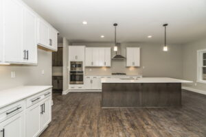 Modern kitchen with white cabinets, stainless steel appliances, dark wood island, and pendant lighting. Features hardwood flooring and neutral wall colors.