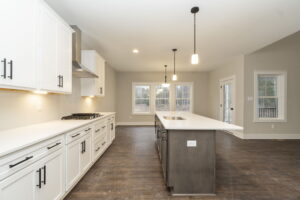 Modern kitchen with white cabinets, dark wood island, and pendant lighting. Features stainless steel appliances and a large window in the background.