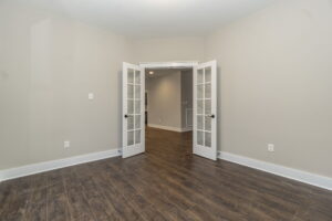 Room with wood flooring, light gray walls, and double French doors opening to another room.