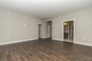 Empty room with light gray walls, dark wood flooring, and two doorways.