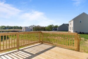 A wooden deck overlooks a grassy area with residential houses and construction in the background, under a partly cloudy sky.