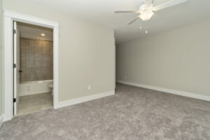 Empty carpeted room with a ceiling fan and open door leading to a bathroom with tiled walls and flooring.