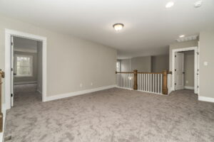 A carpeted upstairs hallway with a wooden railing, a small light fixture, and two open doorways leading to bedrooms.