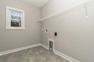 Empty laundry room with gray walls, tiled floor, a single window, and a white wire shelf along the wall.