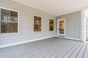 A gray-painted porch with three windows and a glass door leading inside. The ceiling and floor are made of light-colored wood.