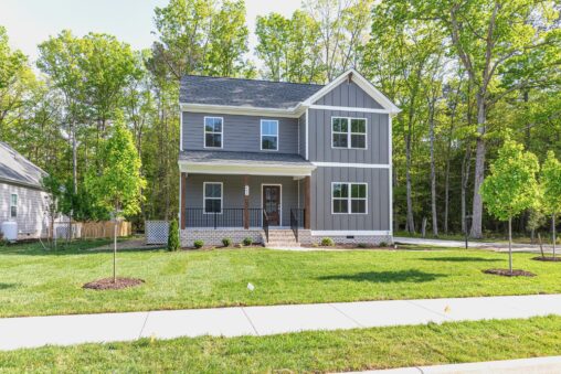 Two-story gray Haley Meadows house with white trim, front porch, green lawn, and trees on a sunny day.