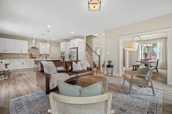 Discover the perfect living space at Haley Meadows, featuring a spacious open area with a brown leather sofa, a modern kitchen, and dining area. The light wood flooring ties the space together beautifully.