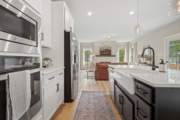 The modern kitchen and living area at Haley Meadows boast a sleek black and white theme, complemented by stainless steel appliances and rich hardwood floors.