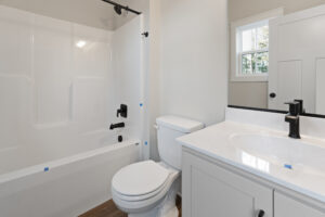 A bathroom with a white bathtub and shower, a toilet, a sink with a black faucet, and a window.