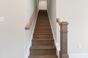 A wooden staircase with a light brown banister ascends between white walls, leading to an upper floor.