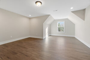 A spacious, empty room with light wood flooring, neutral walls, and a window letting in natural light.