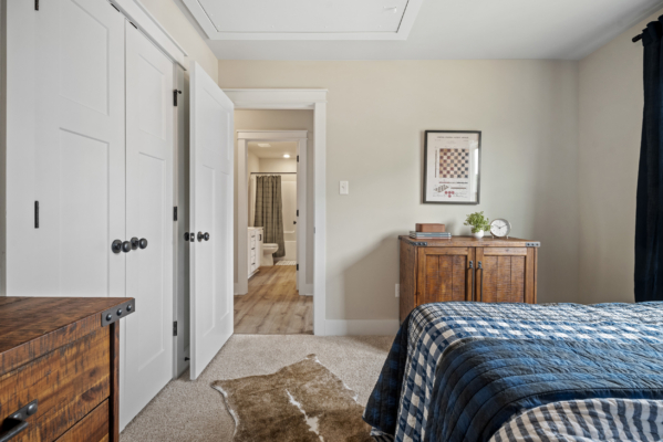 The bedroom in Haley Meadows features elegant wooden furniture, a blue plaid bedspread, open closet and bathroom doors, and soothing beige walls.