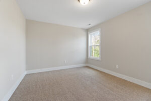 An empty room with Brickshire-inspired beige walls, a carpeted floor, and a window on the right side.
