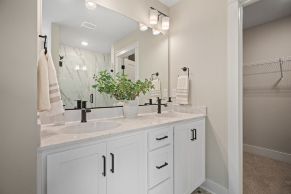 In the sleek Haley Meadows residence, discover a modern bathroom featuring a double sink, elegant black fixtures, a luxurious marble shower, and a potted plant gracing the countertop.