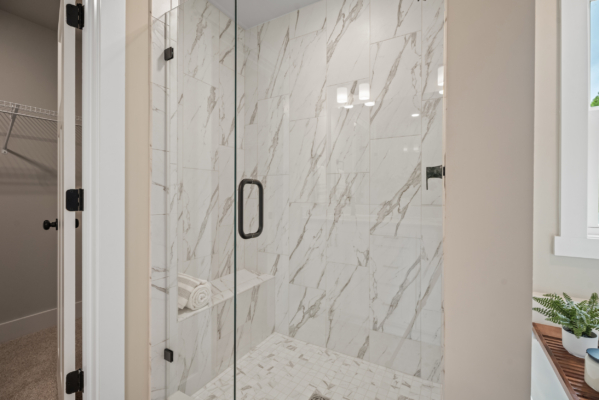 The Haley Meadows bathroom features a modern shower with a sleek glass door, elegant marble tiles, and a plush towel resting on the built-in bench.