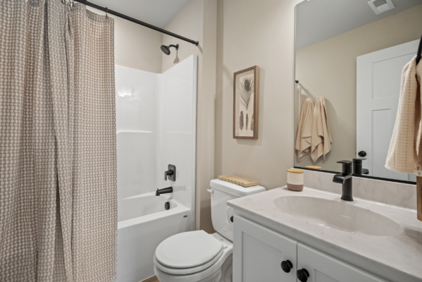 A modern bathroom at Haley Meadows features a shower, curtain, toilet, sink, large mirror, and towels neatly arranged on a rack.