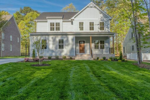 A sunny day highlights a two-story white house with a front porch, nestled among trees and lawns—a charming new home.