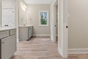 A spacious bathroom with a large mirror, dual sinks, grey cabinets, and wood-look flooring reminiscent of Highland charm. A window provides natural light, enhancing the serene ambiance.