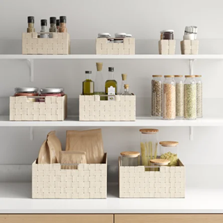 Three white shelves hold baskets and jars of various food items, including grains, oils, and spices. The storage containers are neatly arranged, providing an organized and clean appearance.