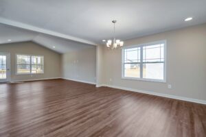A spacious room with hardwood floors and beige walls stands ready for your vision, featuring large windows that let in an abundance of natural light and a chandelier adding a touch of elegance—a perfect base station for launching new ideas or a serene dispatch point for relaxation.
