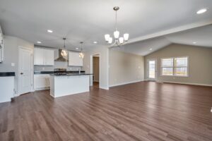 The Carter open-concept living area features beautiful hardwood floors and a modern kitchen with elegant white cabinets, a chic island, and a dazzling chandelier reminiscent of an old-world dispatch station.