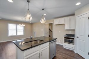 Modern kitchen featuring a central island, pendant lights, stainless steel appliances, and hardwood flooring—perfect for crafting culinary masterpieces like a pro at your own dispatch station.