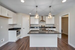Modern kitchen designed by Carter featuring white cabinets, black countertops, an island, stainless steel appliances, and pendant lights.