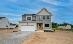 The two-story gray house in Stafford, featuring a white garage and a small front yard, sits gracefully under the blue sky.