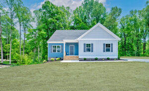 The single-story blue house with white trim, nestled in Maplewood, features porch steps leading to a lush green lawn. Surrounded by tall trees, this charming home offers serene views reminiscent of a quaint dispatch station setting.