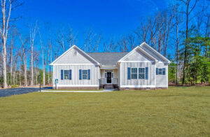 A single-story white house with a gray roof sits peacefully like a dispatch station amidst a grassy lawn and bare trees under a clear blue sky.