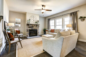 Cozy Westwood living room with neutral tones, fireplace, ceiling fan, and windows with drapes letting in natural light.