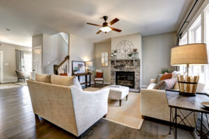 Cozy living room with beige sofas and stone fireplace, nestled in Westwood. A wall clock and ceiling fan complete the space, all illuminated by natural light.