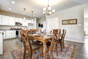 A dining room adorned with a wooden table and chairs, illuminated by a chandelier. White cabinets complement the decor, while a 'Home' sign adds charm. This cozy space feels like your personal station in Westwood.