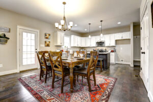Modern dining room with a Westwood wooden table, chairs, and patterned rug; open view to kitchen with white cabinets.