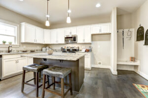 Modern kitchen in Westwood, featuring white cabinets, marble countertops, and an island with two stools. Hanging lights illuminate the area like a dispatch station's glow.