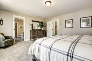 Cozy Westwood bedroom with a plaid bedspread, dresser, armchair, and a view into an adjacent bathroom.