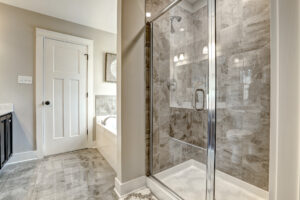Modern bathroom with a glass shower, tiled walls, and floor; the bathtub is visible beside a door on the left. This sleek space feels like a calming station amid the bustle of everyday life.