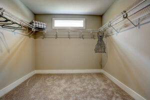 The walk-in closet, reminiscent of a Westwood dispatch station, features beige carpet, wire shelves, and a small window.