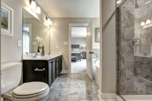 The modern bathroom in Westwood features a double sink, toilet, and glass shower. A doorway seamlessly connects to a bedroom in the background, blending functionality and style like a dispatch station of comfort.