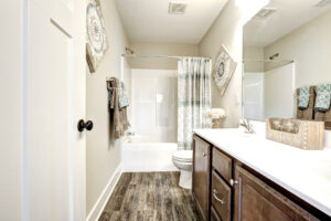 A modern bathroom akin to a stylish station, featuring a bathtub, shower curtain, wooden cabinets, and decorative wall art.