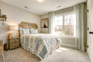 Cozy Westwood bedroom with a rustic wooden bed, patterned bedding, large window with curtains, and soft carpet flooring.