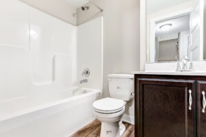 A clean white bathroom in Brickshire features a bathtub, toilet, and a wooden cabinet under the sink.
