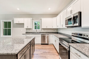 Discover the modern kitchen in Lot 37 at Brickshire, featuring white cabinets, granite countertops, stainless steel appliances, and a large island.