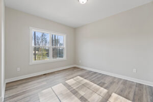 Bright, empty room with a large window overlooking Autumn Hill, featuring gray walls and elegant wood flooring.